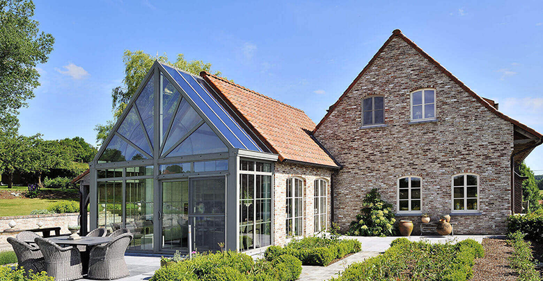 Vue extérieure d'une maison en pierre avec une véranda, et de son jardin. 