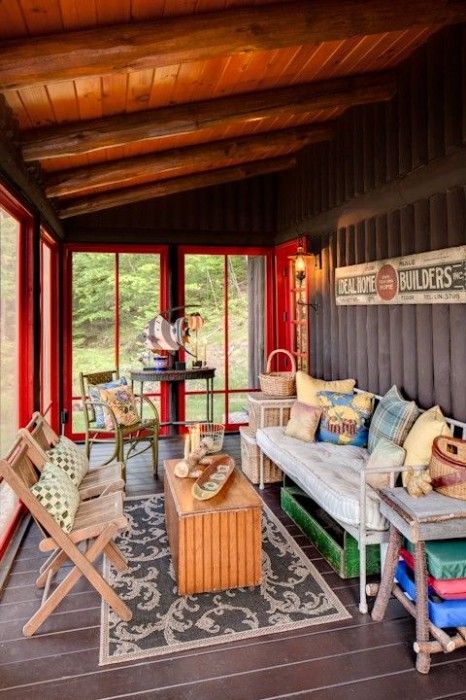 Vue intérieure d'une véranda en bois colorée aménagée en salon avec des meubles et objets de récupération. 
