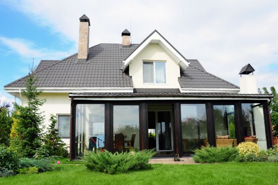veranda en aluminium noir adossé à une villa 4 façade blanche et donnant sur un jardin verdoyant