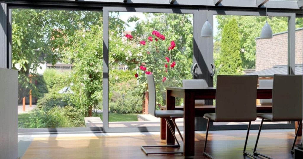 Vue intérieure d'une véranda ouverte sur un jardin fleuri et aménagée en salle à manger avec une table et des chaises design. 