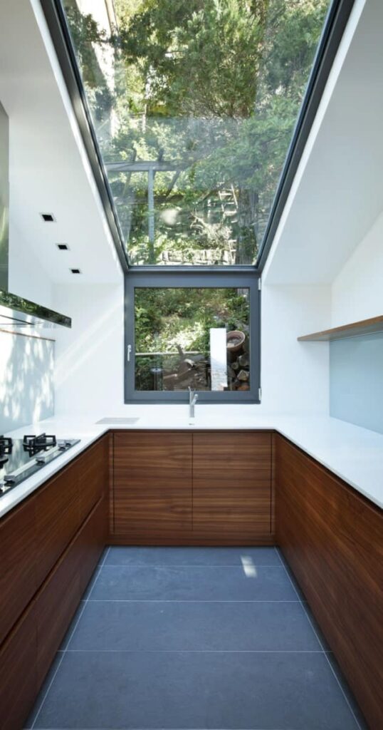 Vue intérieure d'une véranda blanche aménagée en cuisine avec une grande verrière au plafond. 