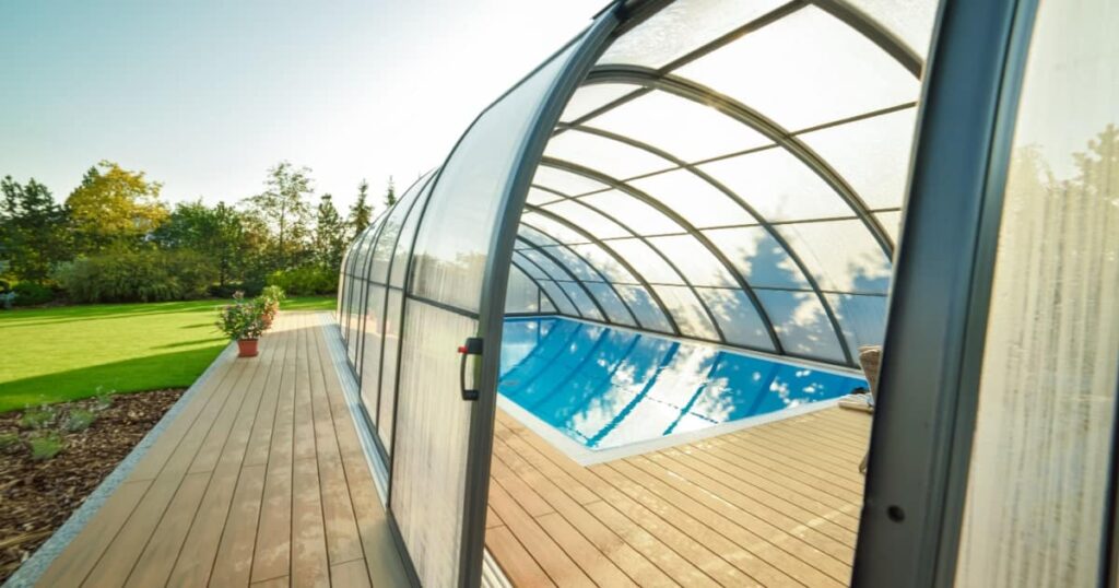 Vue d'un abri rétractable protégeant une piscine dans un grand jardin. 