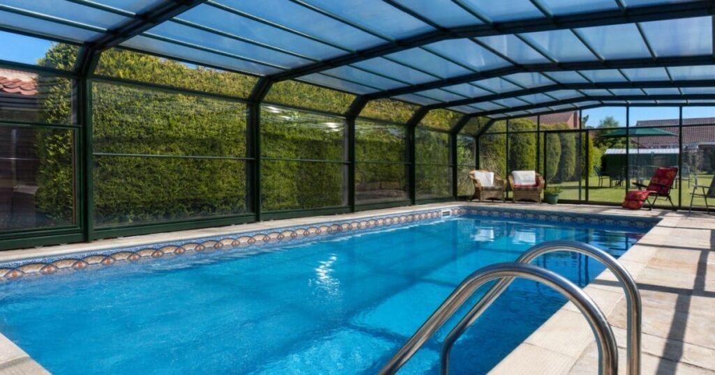 Une piscine sous une véranda avec des chaises de jardin autour.