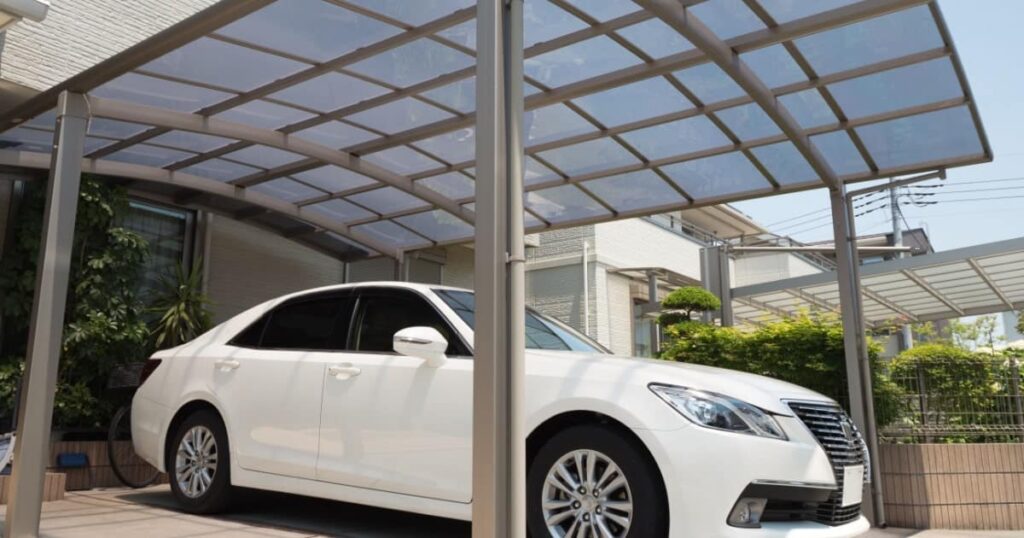 Une voiture blanche abritée sous un haut carport moderne en aluminium et toiture transparente. 