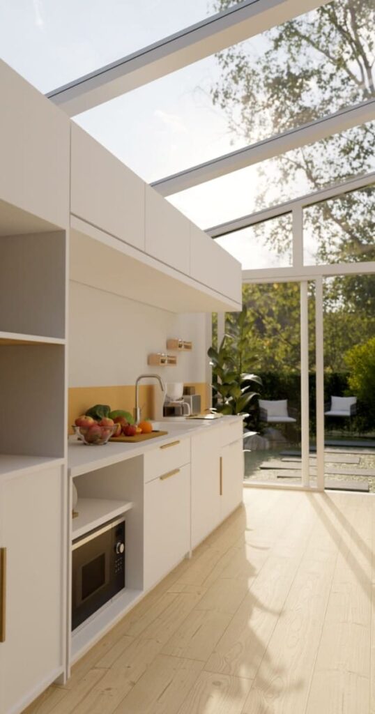 Vue intérieure d'une véranda en longueur aménagée en cuisine, avec des meubles blancs, un parquet en bois clair et une grande verrière au plafond. 
